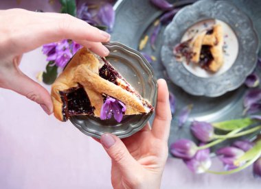 Bir kadının elindeki ahududu katmanlı pasta Tabaktaki leylak bahar laleleri