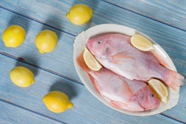 Çiğ pembe tilapia balığı sarı limonlarla çevrili bir tabakta yatıyor. 