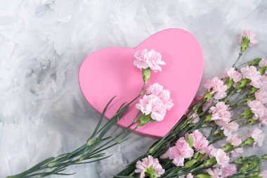 Pembe karanfiller ve açık gri çimento arka planda kalp şeklinde bir kutu. Bir hediye.