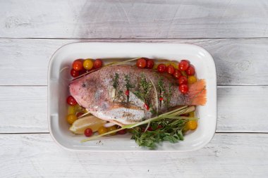 Çiğ kırmızı tilapia balığı otlarla, baharatlarla, kırmızı biberlerle, domateslerle, limonla pişirilir., 