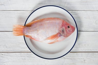 Tabakta çiğ balık, pembe tilapia. Tahta beyaz bir masa, düz bir yiyecek.