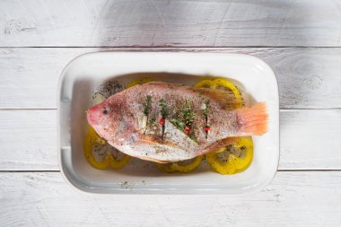 Çiğ kırmızı tilapia balığı otlarla, baharatlarla, kırmızı biberlerle, domateslerle, limonla pişirilir., 