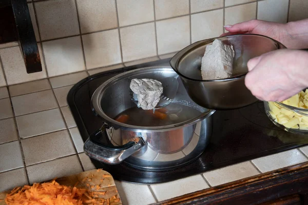 Bir kadın mutfaktaki tavadan haşlanmış eti çıkarır. 