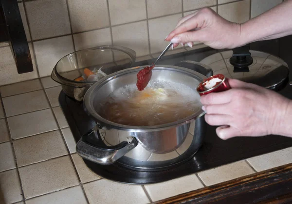 Bir kadın tencereye domates ezmesi koyar. Çorba pişirmek için malzemeler.