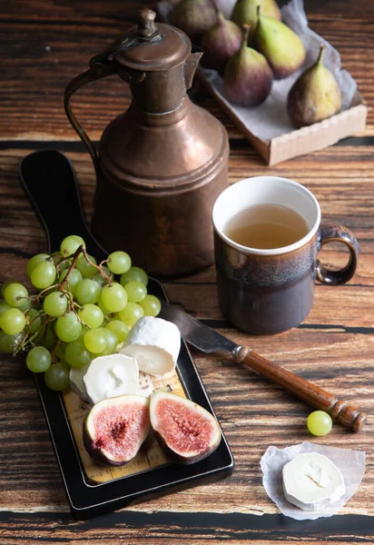 Cheese plate with goat cheese, grapes and figs, copper teapot, angle view — Stock Photo, Image