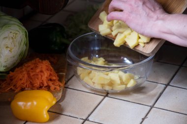 Bir kadın mutfakta taze sebzelerin arka planında patates kesiyor. Aşama aşama çorba yapmak için gerekli malzemeler. Yüksek kalite fotoğraf