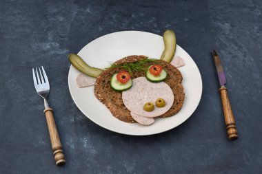 Tabakta siyah ekmek, sosis ve sebzelerden oluşan neşeli bir boğa portresi şeklinde, karanlık bir arka planda, thuja ve kutsal dallardan oluşan bir dekor. Yüksek kalite fotoğraf