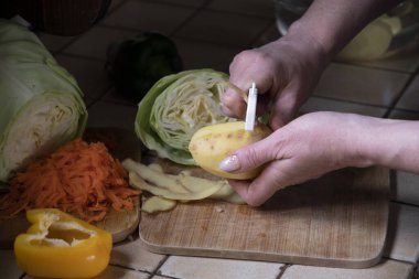 Bir kadın mutfaktaki patatesleri taze sebzelerin arka planına karşı soyar. Aşama aşama çorba yapmak için gerekli malzemeler. Yüksek kalite fotoğraf
