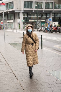 Brüksel Belçika - 01.31.2021, yağmurlu havada Brüksel caddesinde kapüşonlu ve maskeli bir kadın yürüyor. Yüksek kalite fotoğraf