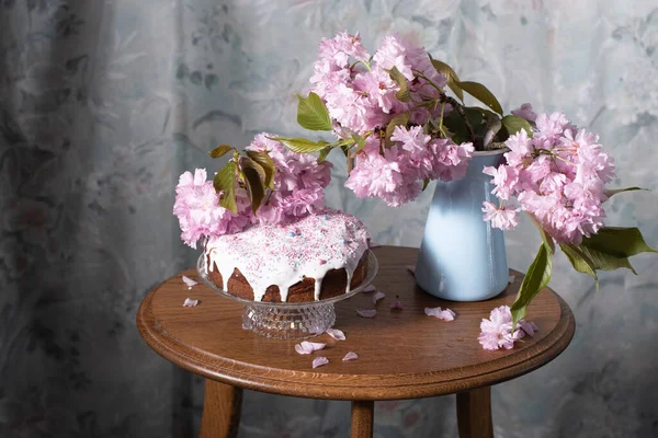 Easter cake and painted eggs and a bouquet of pink sakura flowers on a table in a decorated spring room, a beautiful still life. High quality photo