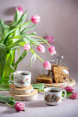 Hayat, erken bahar kahvaltısı konsepti kahve, çay ve bir buket lale ve nergis çiçeğinin arka planında kek.