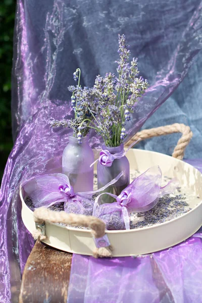 Lilac lavender in vases and lavender sachets in chiffon bags on a tray with dry flowers, aromatherapy, purple background, floral still life. High quality photo