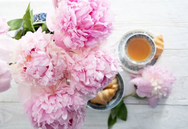 spring still life with croissants and a bouquet of pink luxurious peonies in an ancient Chinese vase with blue ornament, an antique tea cup, early breakfast or brunch, High quality photo
