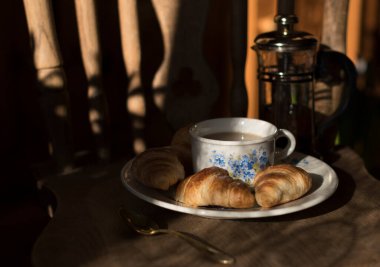 fresh mini croissants for morning breakfast on a plate with a cup of coffee with blue forget-me-nots, vintage still life on a chair. High quality photo