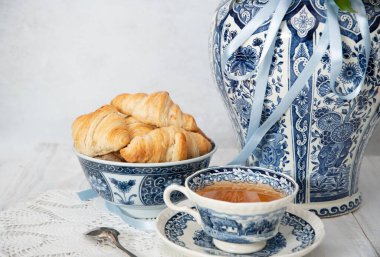 spring still life with croissants and a bouquet of pink luxurious peonies in an ancient Chinese vase with blue ornament, an antique tea cup, early breakfast or brunch, High quality photo