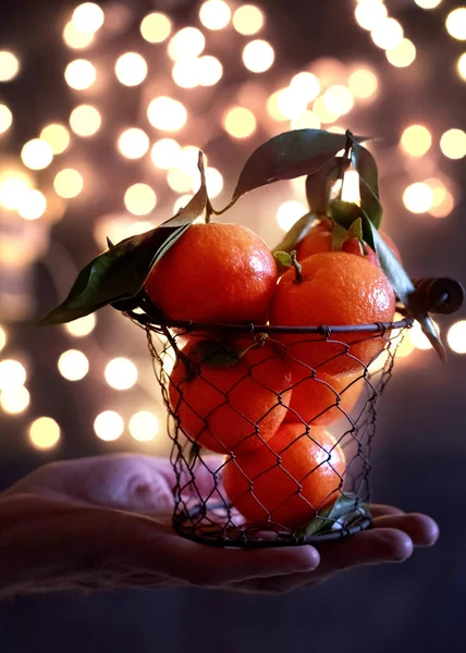 tangerines in a mesh bucket on a male hand against a background of bright yellow bokeh, New Years mood. High quality photo