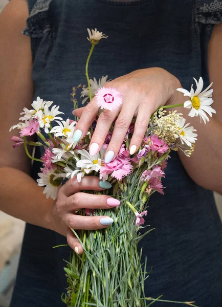 a young woman with a beautiful summer manicure holds a bouquet of wild flowers in pastel shades. High quality photo