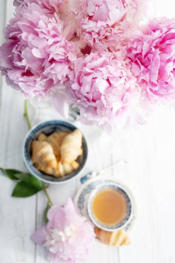 spring still life with croissants and a bouquet of pink luxurious peonies in an ancient Chinese vase with blue ornament, an antique tea cup, early breakfast or brunch, High quality photo