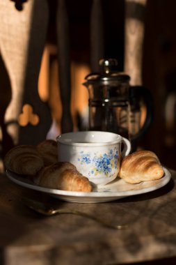 fresh mini croissants for morning breakfast on a plate with a cup of coffee with blue forget-me-nots, vintage still life on a chair. High quality photo