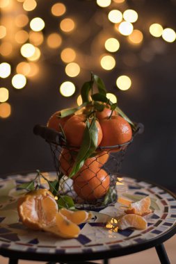tangerines in a mesh bucket on a table against a background of bright yellow bokeh, New Years mood. High quality photo