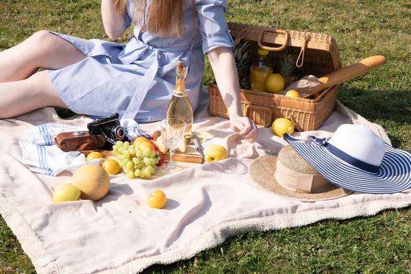 a young woman in a blue dress and straw hat is resting on a picnic with fruits, cheese plate and champagne, rest from worries and household chores parks and recreation areas,.High quality photo