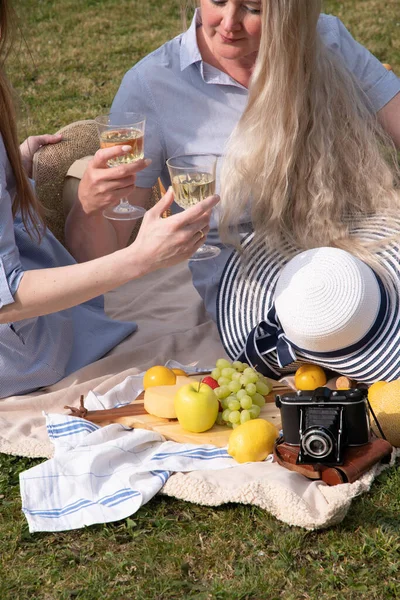 a two young women in a summer long dresses is resting on a picnic, a Blanket with cheese plate and fruits, rest from worries and household chores, parks and recreation areas,.High quality photo