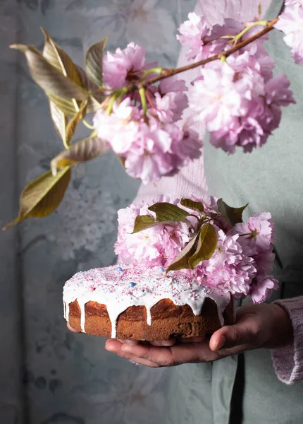 a woman decorates a homemade Easter cake with pink sakura flowers, spring blossom, a bouquet of pink sakura flowers on a table in a decorated spring room, a beautiful still life. High quality photo