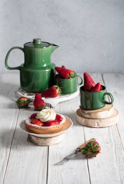 Meyveli, çilekli ve yeşil çay takımlı bir hayat kremalı çilekli pasta, bir kadın eli tatlı çatalıyla bir dilim pastayı kırar. Yüksek kalite fotoğraf