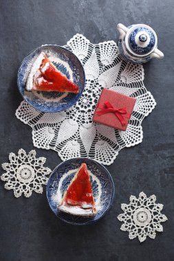 Mavi tabakta kırmızı çilekli Noel turtası ve masada kırmızı bir kutuda hediye, bembeyaz örülmüş peçetelerin üzerinde bembeyaz renkli yiyecekler, kar taneleri şeklinde, kış havası. Yüksek kalite fotoğraf