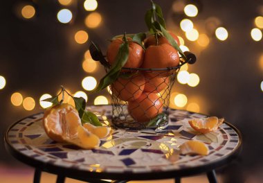 tangerines in a mesh bucket on a table against a background of bright yellow bokeh, New Years mood. High quality photo