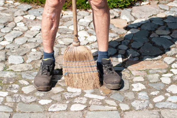 gardener in dirty work clothes and boots holds garden tools, plastic brush broom, seasonal spring work in the garden. High quality photo