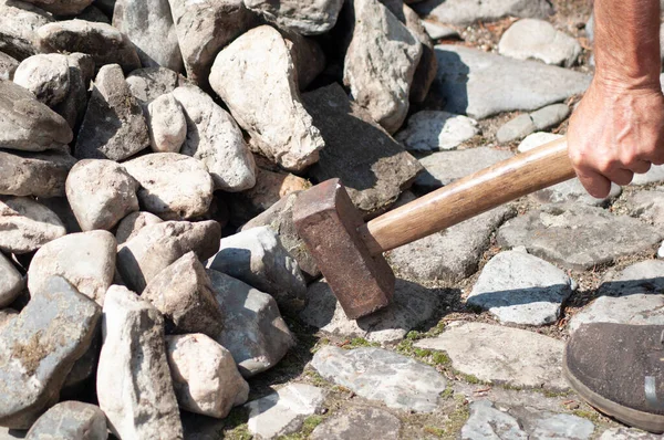 a gardener in dirty work clothes and boots holds a two-bladed iron hammer for working with stones. High quality photo