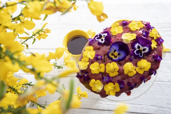 delicious cake decorated with yellow purple pansy flowers on a white wooden table against the background of a bouquet of yellow flowers. High quality photo