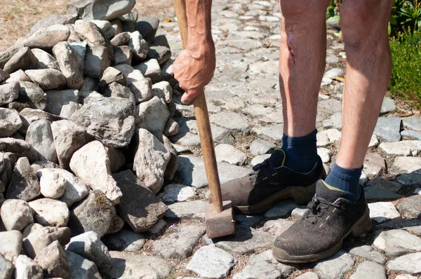 a gardener in dirty work clothes and boots holds a two-bladed iron hammer for working with stones. High quality photo