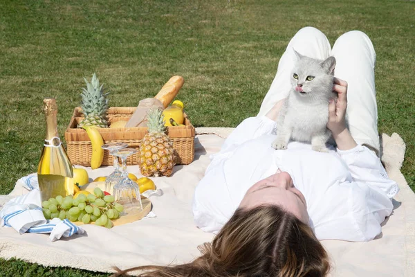 a young woman in a white shirt is resting on a picnic with her pet kitten, rest from worries and household chores, parks and recreation areas,. High quality photo