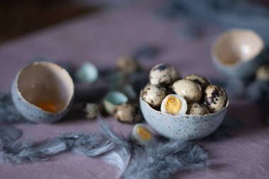Seramik vazolarda bıldırcın yumurtaları, masada gri tüyler, Paskalya natürmortu, doğal besin, diyet ve antioksidan, karanlık anahtar ve sığ alan derinliği. Yüksek kalite fotoğraf