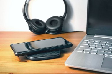 Ofisteki ahşap masadaki kablosuz şarj cihazına şarj olan cep telefonunun yakın plan fotoğrafı. 