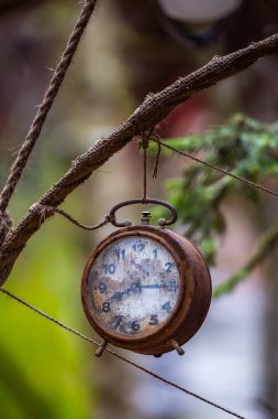 Bahçeye süs olsun diye asılmış eski ve paslı çalar saat. Fotoğraf, düşük ışık koşullarında çekildi. Bulanık arkaplan.