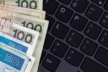 Siyah dizüstü bilgisayar klavyesine yerleştirilmiş Polonya 50 ve 100 PLN banknot seti. Fotoğraf yapay, yumuşak ışık altında çekildi