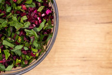 Cam bir kaseye yerleştirilmiş taze, doğranmış pancar yaprakları. Fotoğraf yapay, yumuşak ışık altında çekildi.