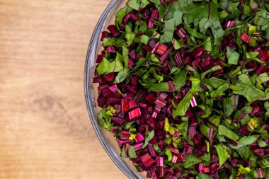 Cam bir kaseye yerleştirilmiş taze, doğranmış pancar yaprakları. Fotoğraf yapay, yumuşak ışık altında çekildi.