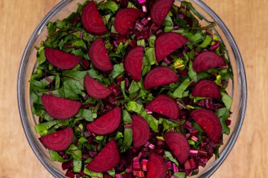 Taze, kesilmiş yapraklar ve cam bir kaseye yerleştirilmiş pancar parçaları. Fotoğraf yapay, yumuşak ışık altında çekildi.