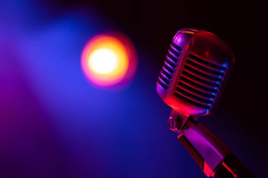 Klasik sahne mikrofonu. Renkli ışıkla aydınlatılmış nesne. Arka planda, sahnedeki bulanık ışık manzarası.