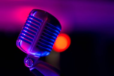 Klasik sahne mikrofonu. Renkli ışıkla aydınlatılmış nesne. Arka planda, sahnedeki bulanık ışık manzarası.