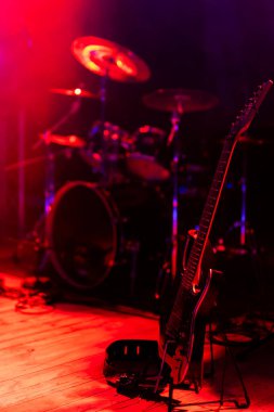 Sahneye yerleştirilmiş siyah bir elektro gitar. Denek güçlü kırmızı ışıkla aydınlatıldı..