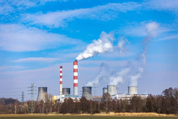 Kömürle çalışan bir enerji santralinin uzaktan görüşü. Tüten bacalar ve soğutma kulelerinden çıkan buhar. Fotoğraf güneşli bir günde çekildi, kontrastlı aydınlatma.
