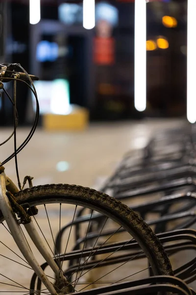 Şehir merkezindeki bisiklet parkına park etmek için kullanılan eski ve kirli dağ bisikleti. Akşam çekilen fotoğraf, zayıf ışık sokak ışıklarını oluşturur..