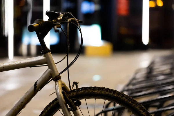 Şehir merkezindeki bisiklet parkına park etmek için kullanılan eski ve kirli dağ bisikleti. Akşam çekilen fotoğraf, zayıf ışık sokak ışıklarını oluşturur..