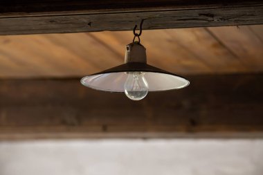 Terk edilmiş ahşap bir evin tavanında eski bir elektrik lambası. Fotoğraf düşük ışık koşullarında çekildi.