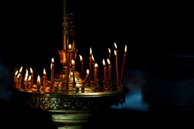 Ortodoks Kilisesi 'nin karanlığında yanan mumlarla dolu bir şamdan. Fotoğraf çok kötü ışıklandırma koşullarında çekildi..